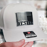 White cap with 'RESIST' and American flag design held by a hand.